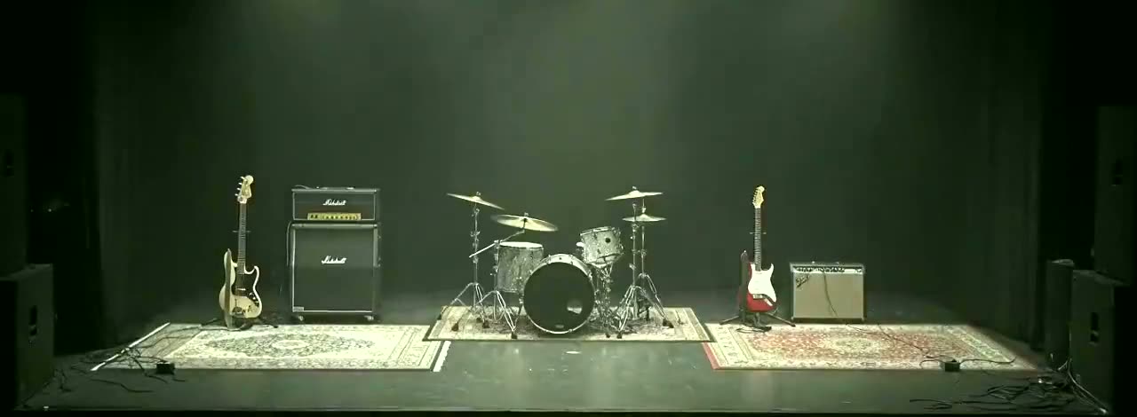A small stage set with drums, guitars and backline, haze in the air.