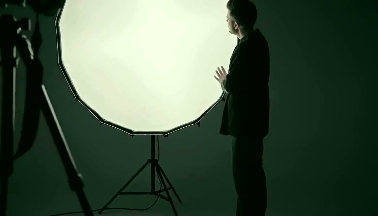 A photographer adjusting a studio light beside a camera on a tripod.
