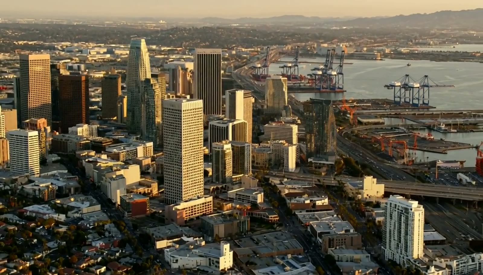 Downtown San Diego at golden hour: towers, freeway movement and the working port beyond the bay.